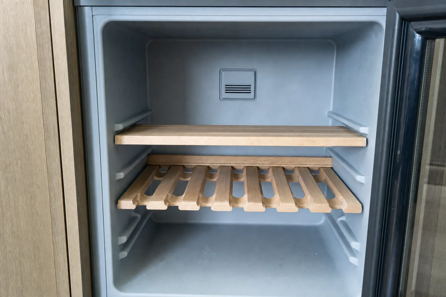 Empty wine cabinet interior with two wooden racks, a rear air vent and the glass door standing open